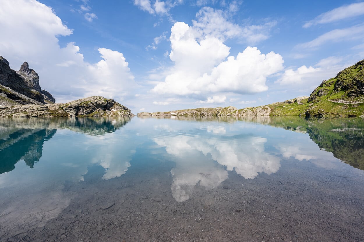 cliuds reflecting in a seren image of an alpine lake on a suny summer day,