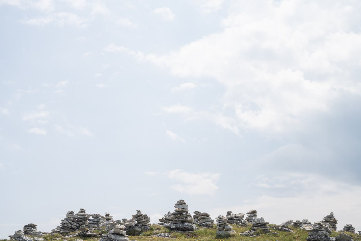 mountain cairns atop a small hill under a partly cloud sky, on a day with soft light