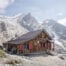 Rifugio Mezzalama on a bright sunny day, the arrival of a long hike in Val d'Ayas, with people outside the hut and glaciers perched on the mountains in the background.