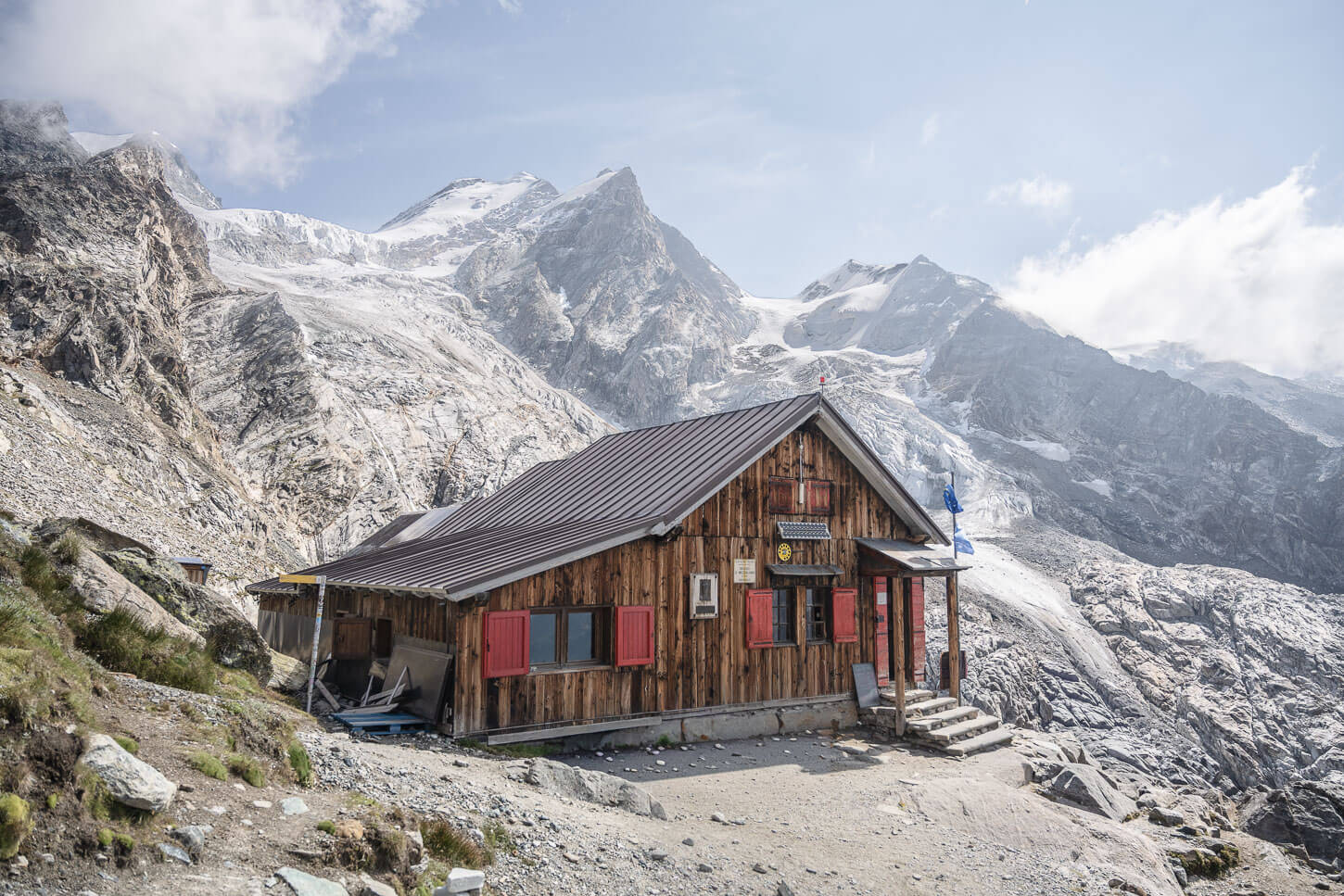Rifugio Mezzalama on a bright sunny day, the arrival of a long hike in Val d'Ayas, with people outside the hut and glaciers perched on the mountains in the background.