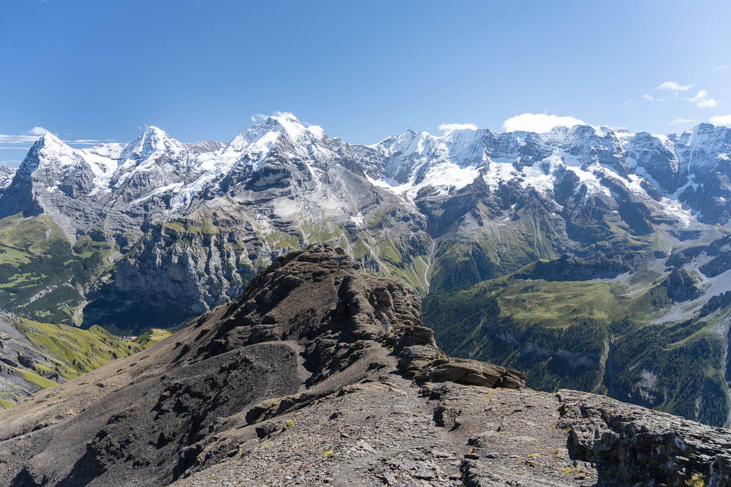 Rocky ledge on the Schilthorn hiking trail, facing the most iconic peaks of the Bernese Oberland, the Eiger, the Monch,and the Junfrau, under a vibrant blue of a sunny sumer day.