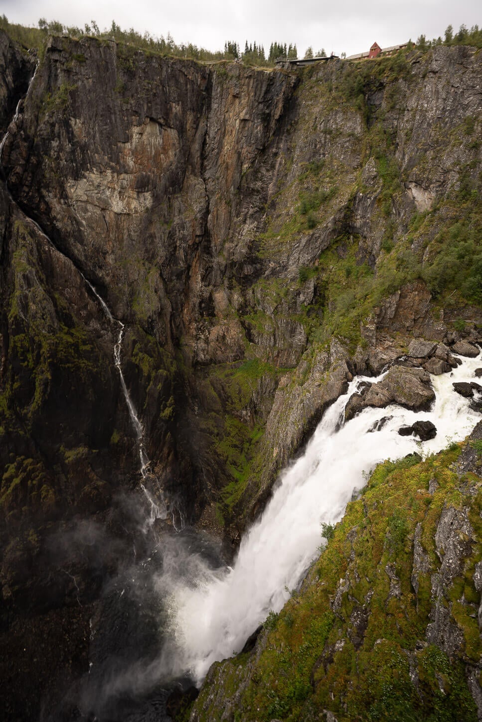 Vøringsfossen from the Hovedutsiktspunkt Fossatromma viewpoint, with the fossly hotel in the background, and the water crashing in the valley down below in a dramatic drop.