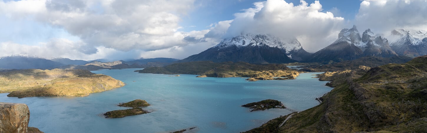 Panoramic image of Lago Pehoé in the morning, with golden light and partially cloudy skies.