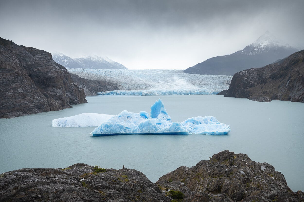 Mirador Glacier Grey lookout on a cloudy day, with an iceberg floating in a lagoon in front of Glacier Gray, under a moody sky,