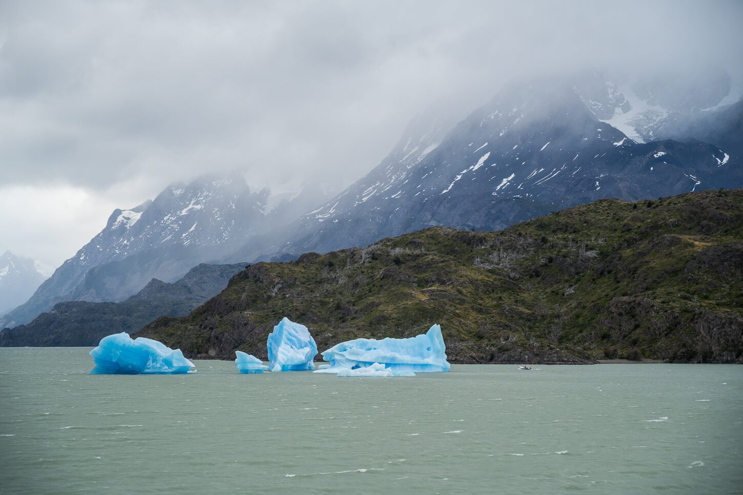 Icebergs floating in Lago Grey in from of Mirador de los Hielos, with a boat passing by and looking tiny in comparison.