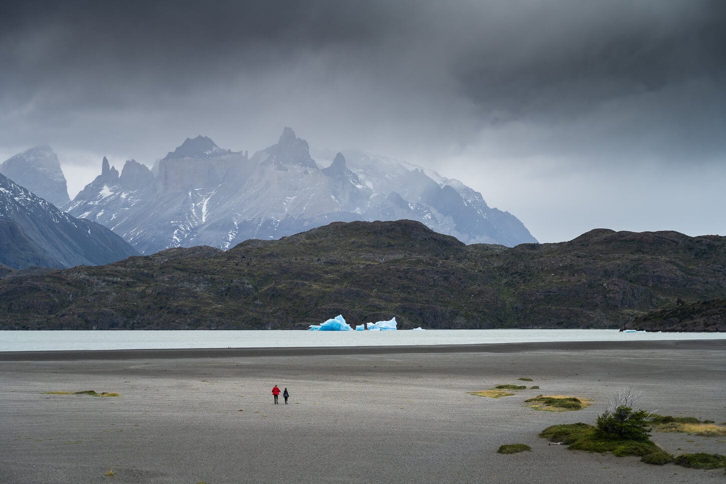 Hikers walking on the beach of Lago Grey to Mirador de los Hielos, under a cloudy sky