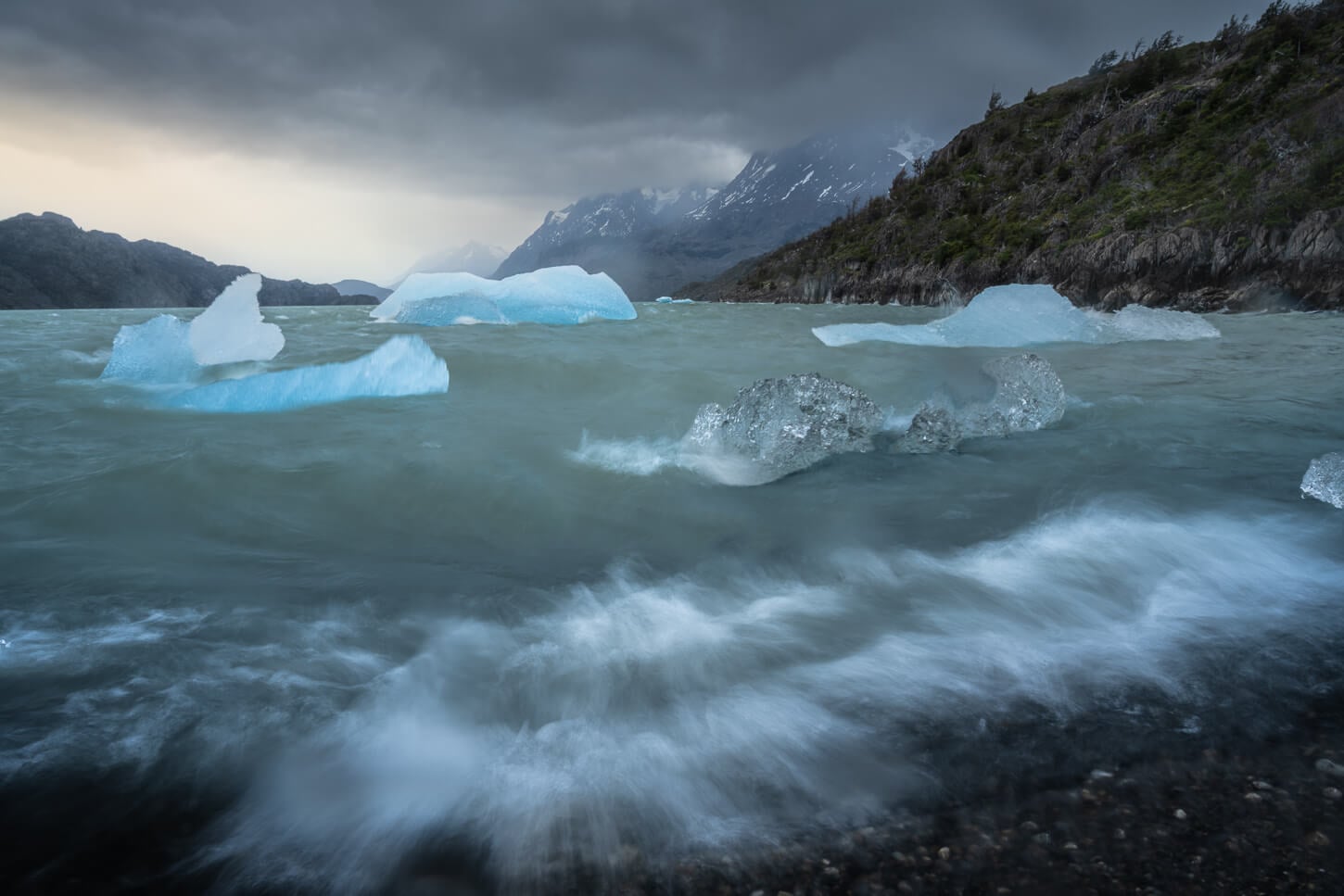 Long exposure photos of Icebergs near Mirador de los Hielos, with the blue color of the ice creating a striking contrast with the dark, cloudy sky.