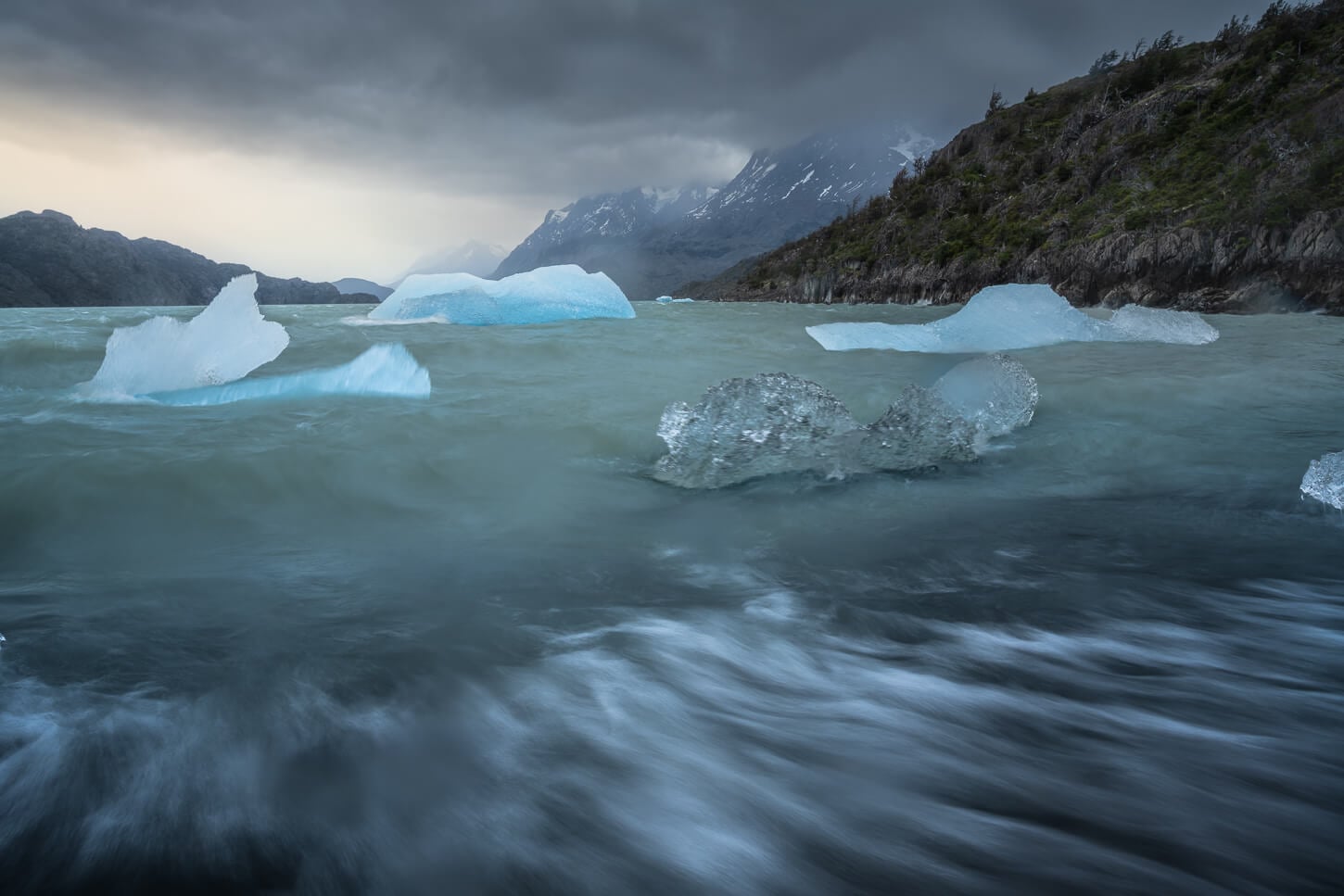 Long exposure photos of icebergs in Patagonian lake, under a moody and dramatic cloudy sky.