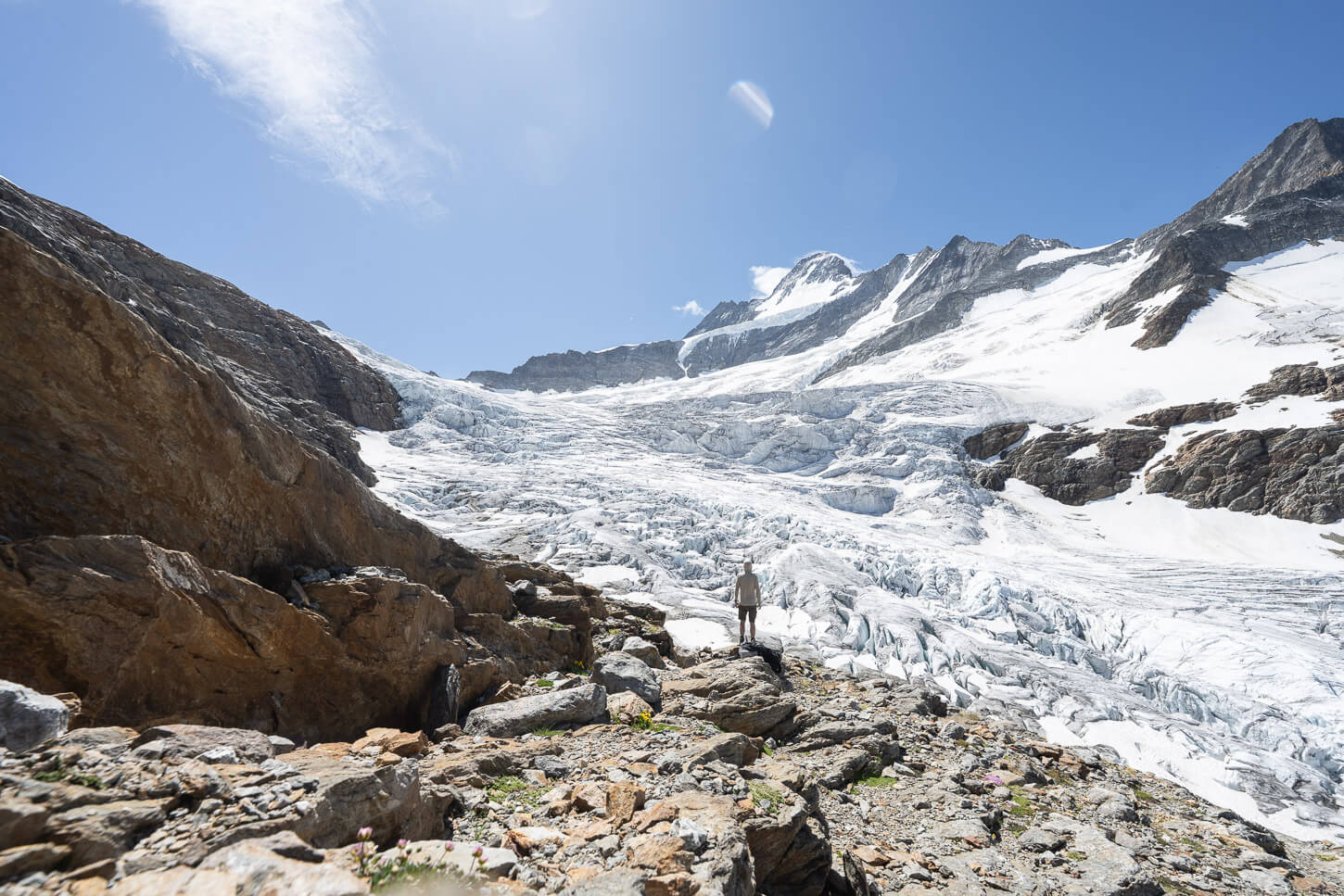 Hiker in front of the vast expanse of Ice og the Upper Grindelwald glacier, on a warm, sunny summer day.