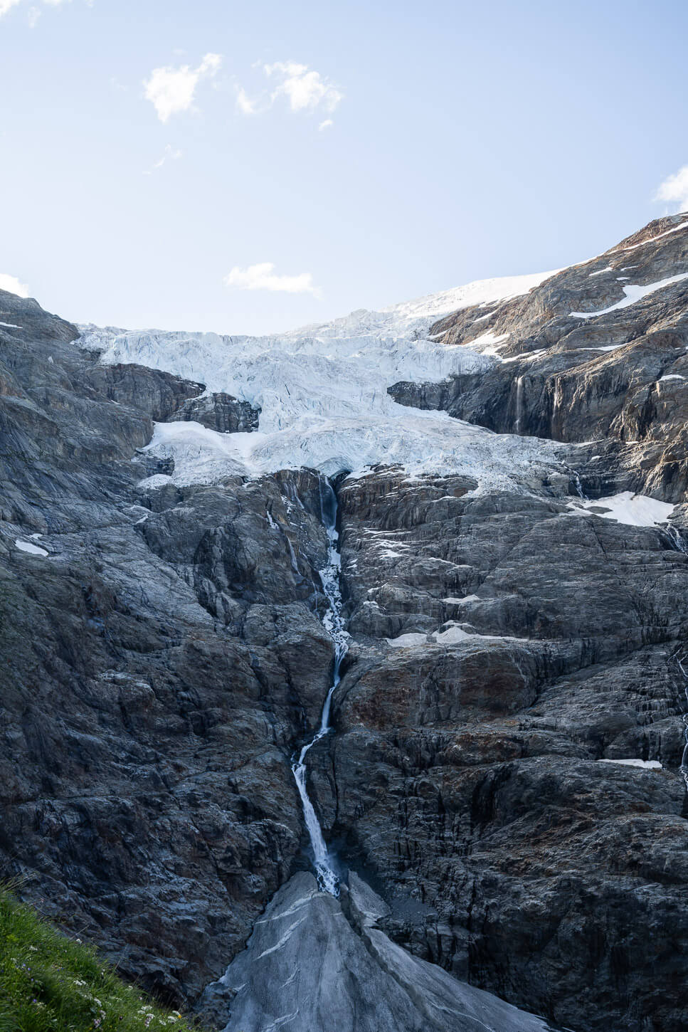 Upper grindelwald glacier's tongue that is visible at 5 kilometers into the hilke., with the massive glacier aboce and a tall waterfall that comes out of it.