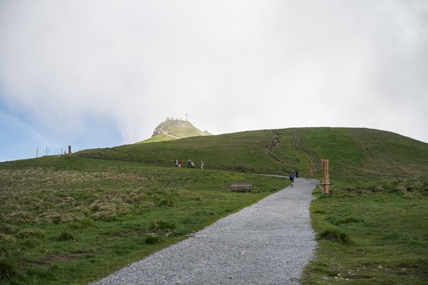 View of Männlichen's summit in the distance, partly covered in clouds, from a gravel road that leads to the panoramic endpoint of the hike.