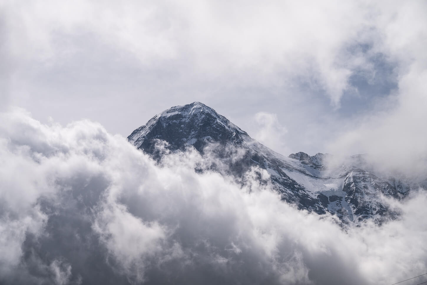Image of a dramatic landscape with a mountain peak rising above a dense layer of clouds.