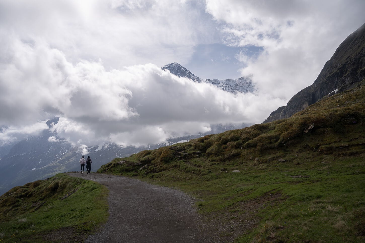 Part of the Panorama trail, from Männlichen to Kleine Scheidegg and Wengen with two hikers doing the hike immersed in the panoramic views of the mountain landscape.