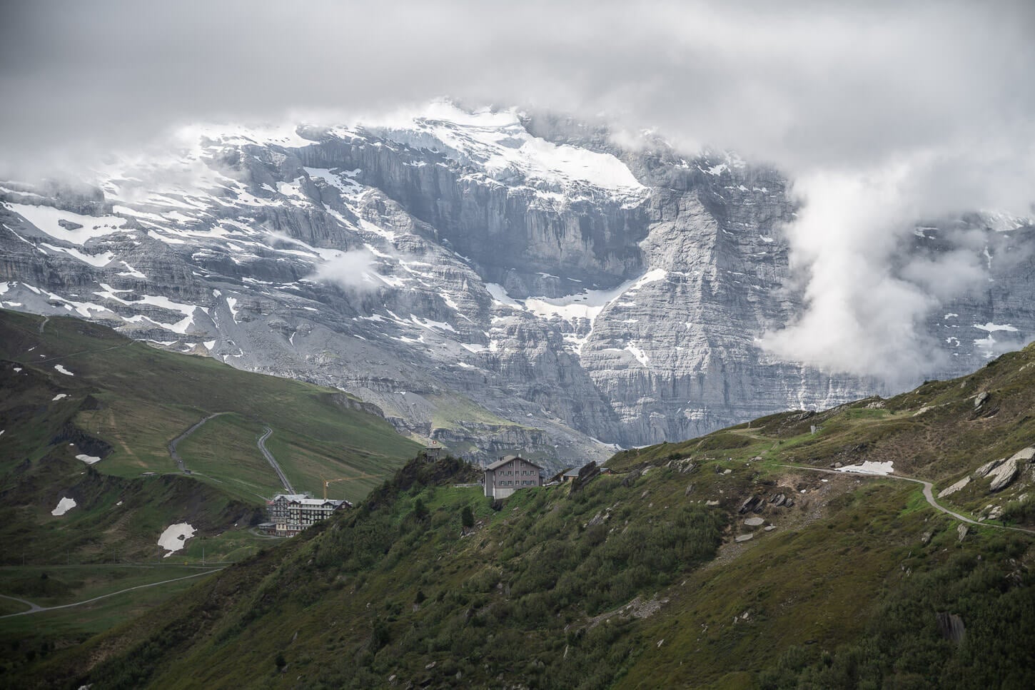 Berggasthaus Stöcki-Grindelwaldblick, panoramic viewpoint of the hike to Lauberhorn and Wengen, under a cloudy sky that still reveals part of the Eiger Rock face with its glaciers.