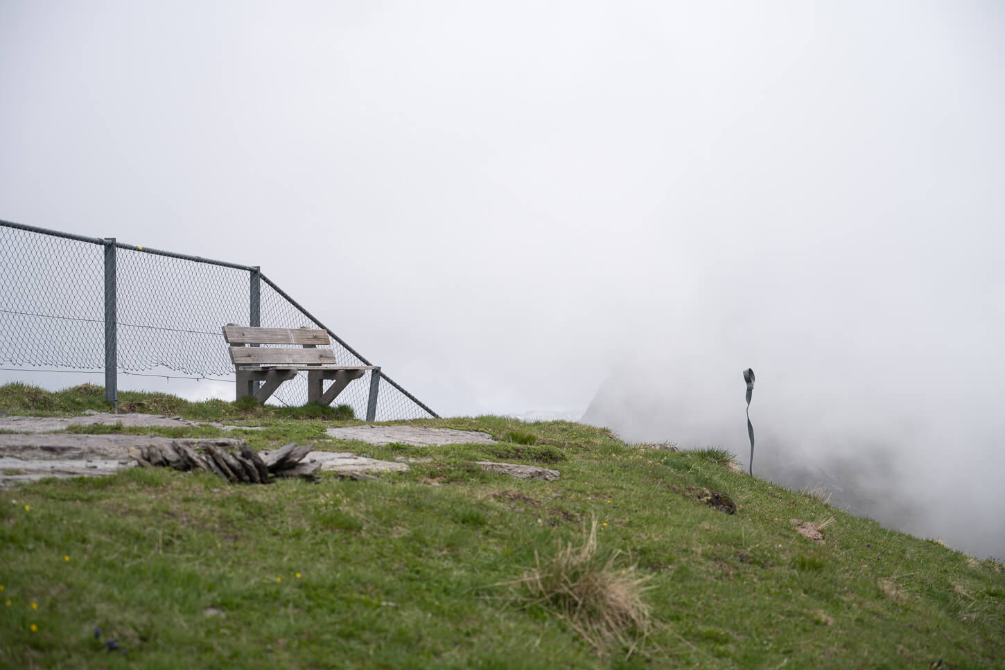 Lauberhorn's summit in the fog with a bench and a small metal sculpture planted in the ground