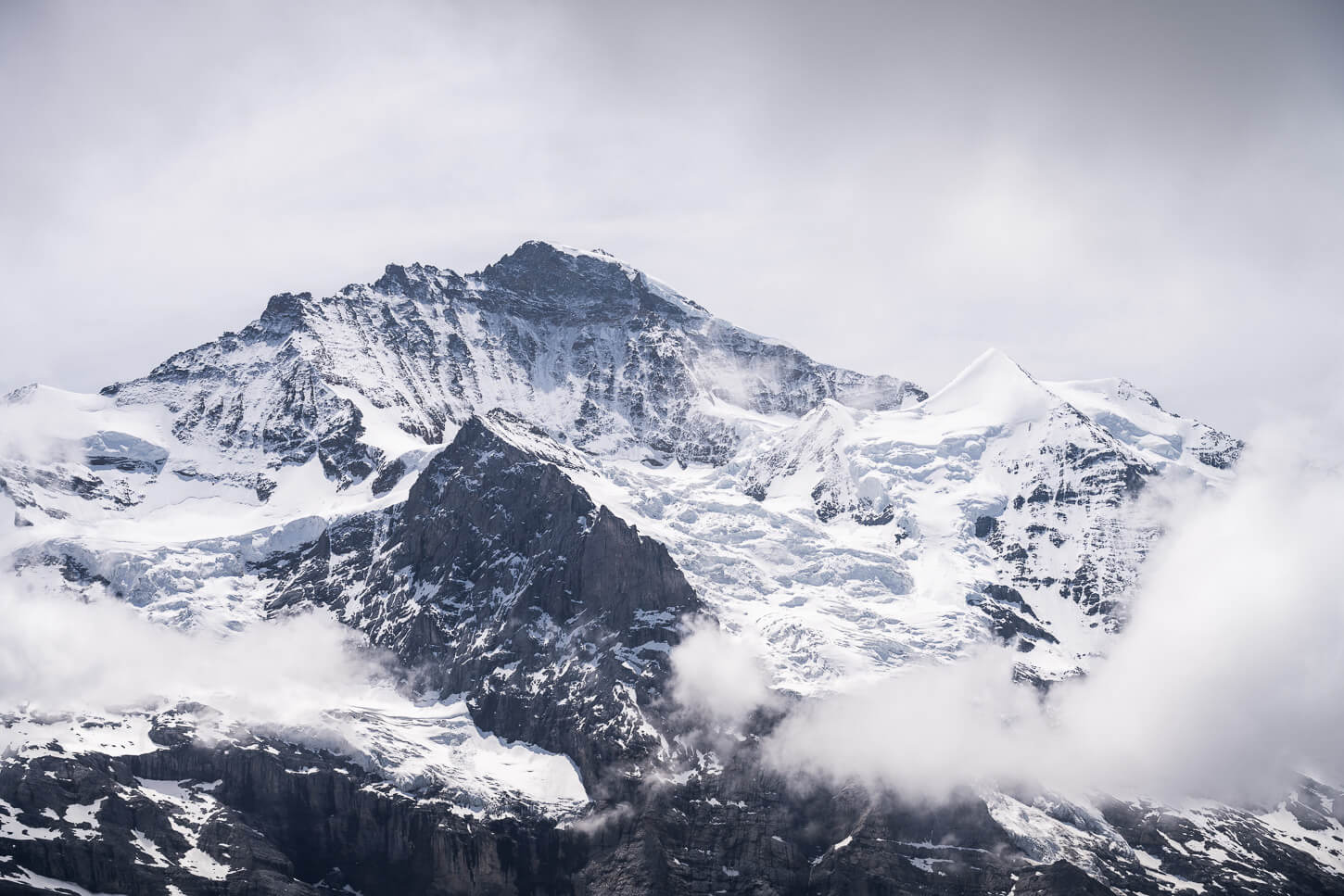 View of the Jungfrau (4,158 m) from Lauberhorn, under a dramatic, cloudy sky with some light that highlights the glacier.