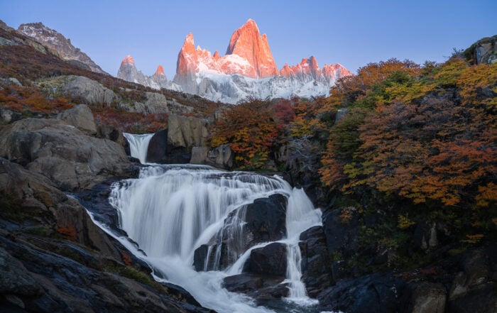 View of El Chaltén's Hidden Waterfall, which makes for a spectacular sunrise hike in Patagonia, with the warm light of the rising sun hitting Mount Fitz Roy, above the hidden waterfall.