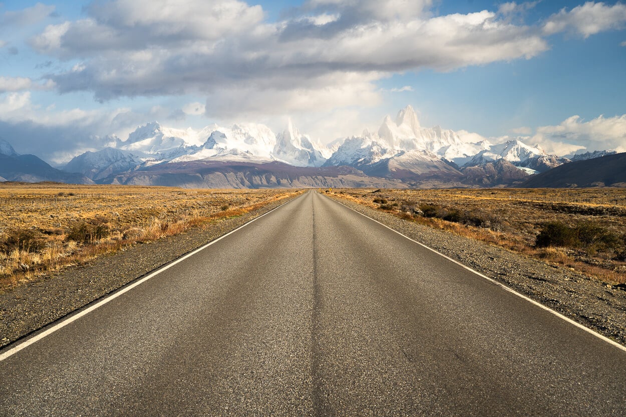 Road leading to El Chaltén, Argentina's Trekking Capital on a sunny day, with snow covered mountains in the distance