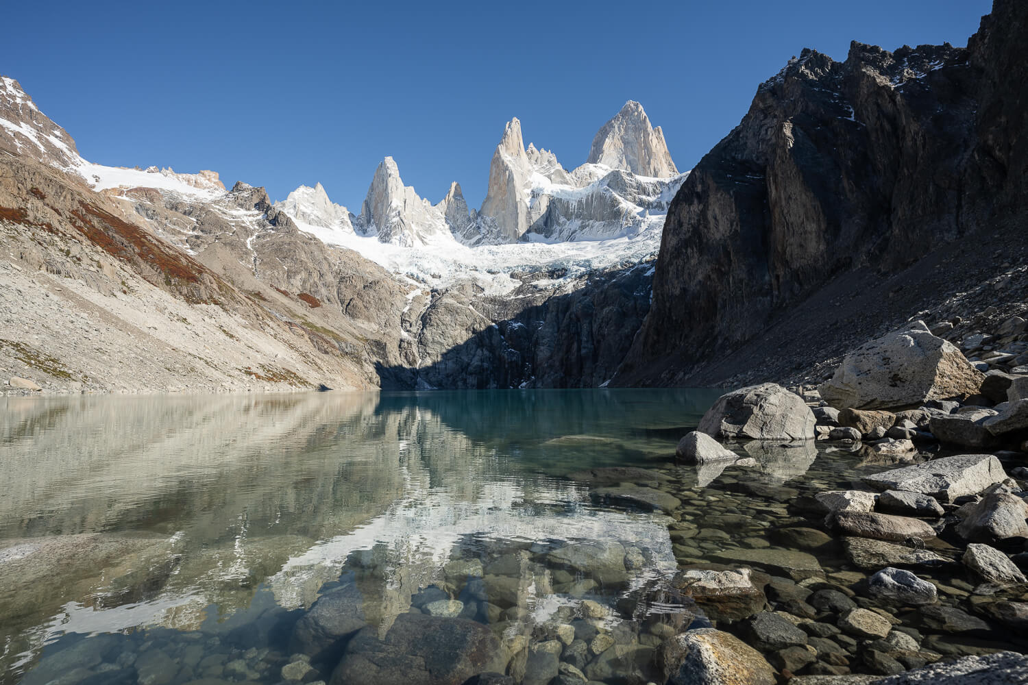 View of Laguna Sucia at the end of the hike, where the mountain Fitz Roy reflects in the waters of the lake on a sunny day with blue skies.