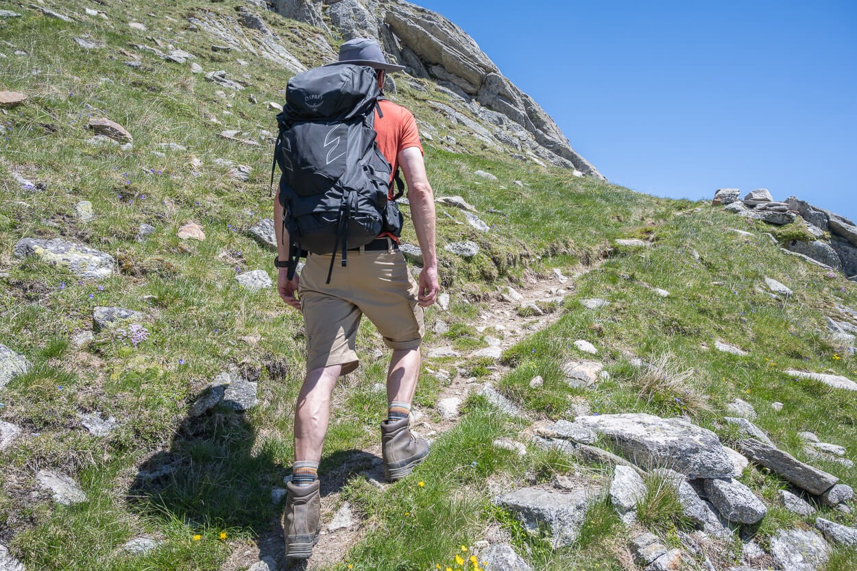 Hiker with an Ospery Talon backpack on the back, hiking up a mountain in summer.