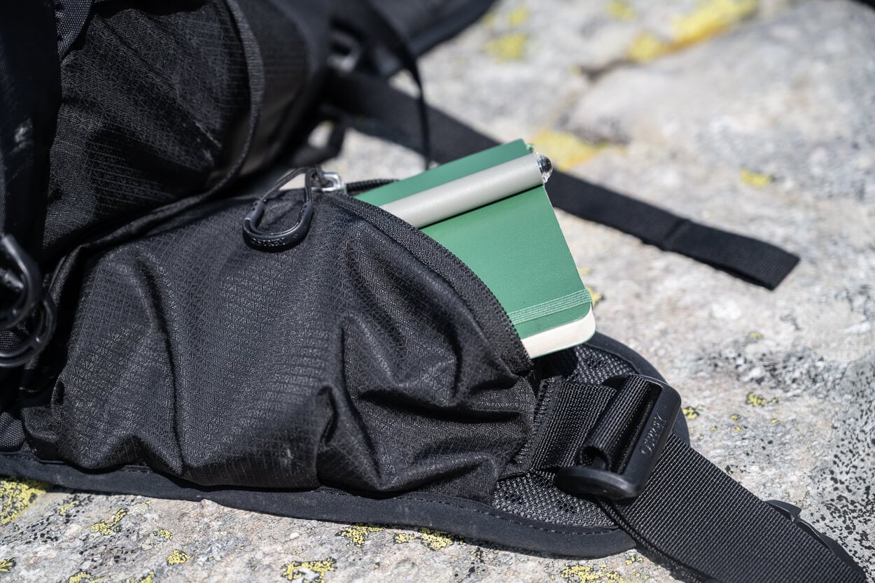 Notepad partly inserted in a hipbelt pcket of a backpack.