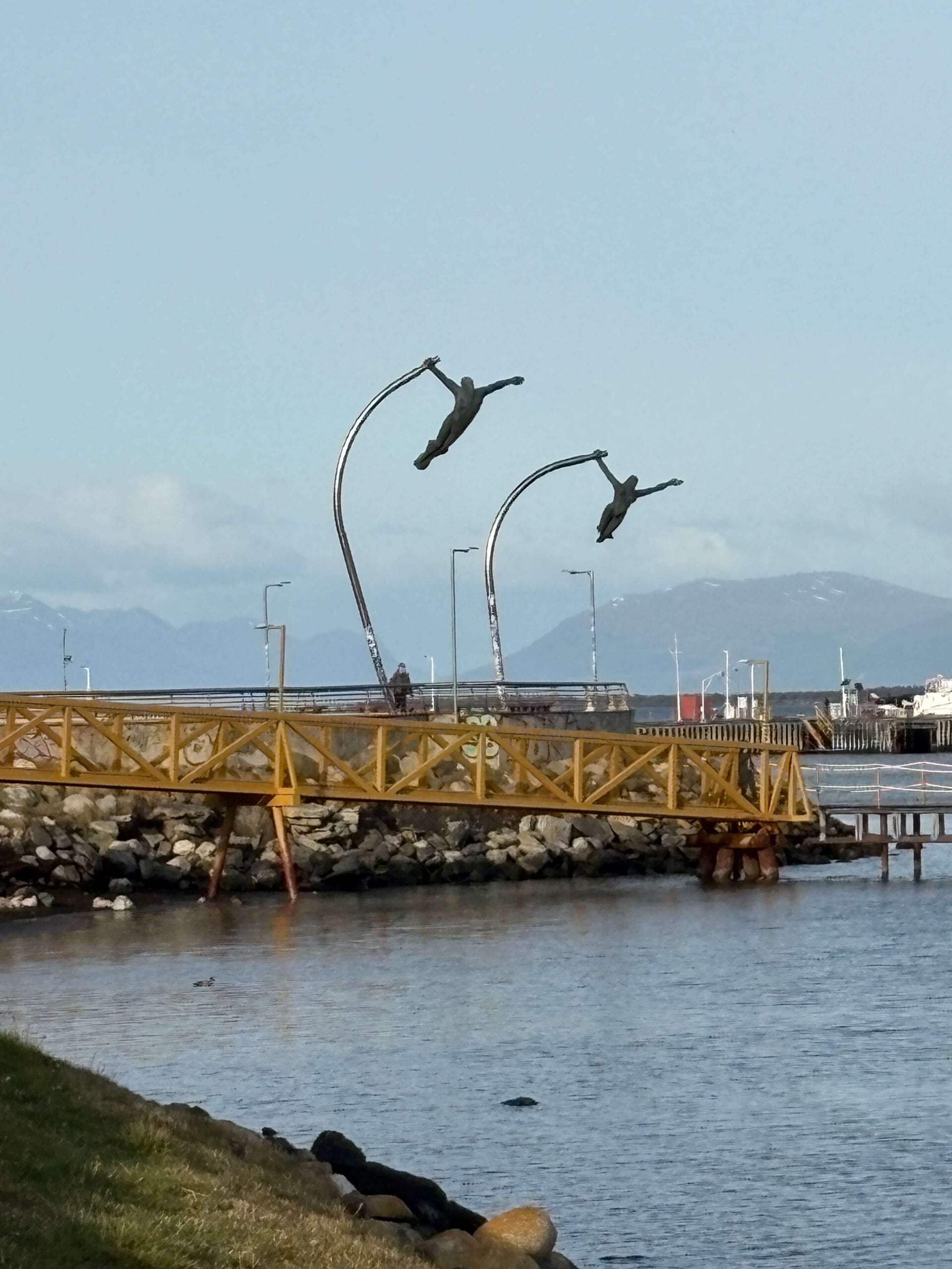 Monumento al Viento sculpture in Puerto Natales. where two human figures ata hanging on to a pole.