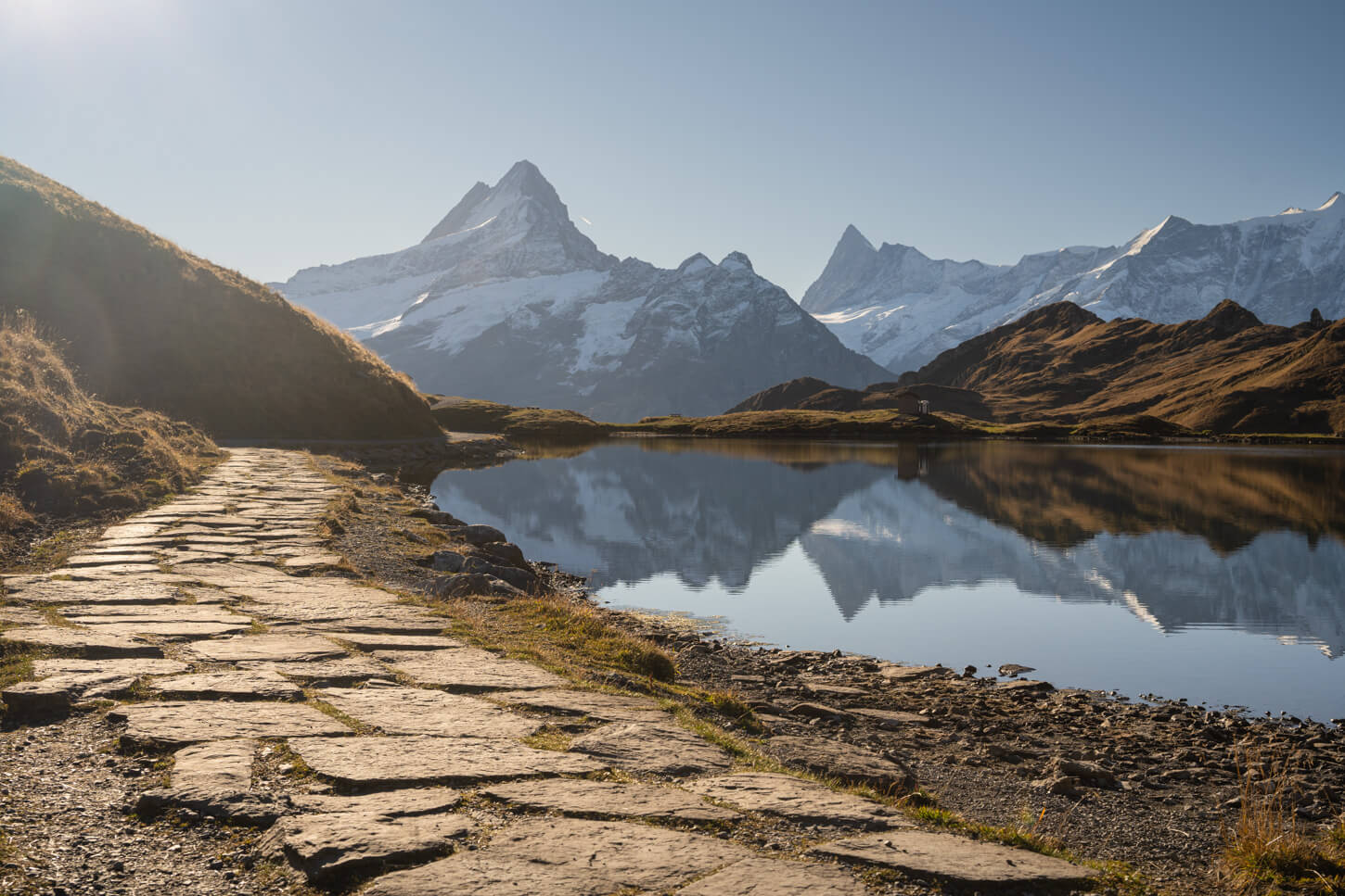 Stone hIking path next to the Bachalpsee lake, with mountains reflecting in the lake.