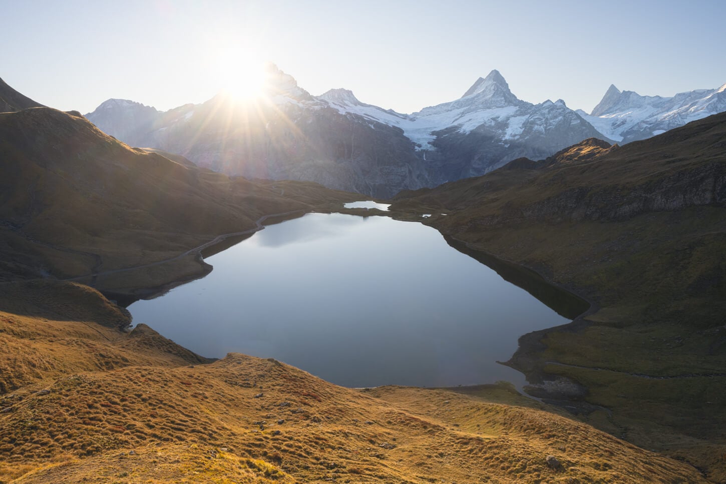 Bachalpsee at sunrise with the sun peaking above the mountains and flooding the landscape with light