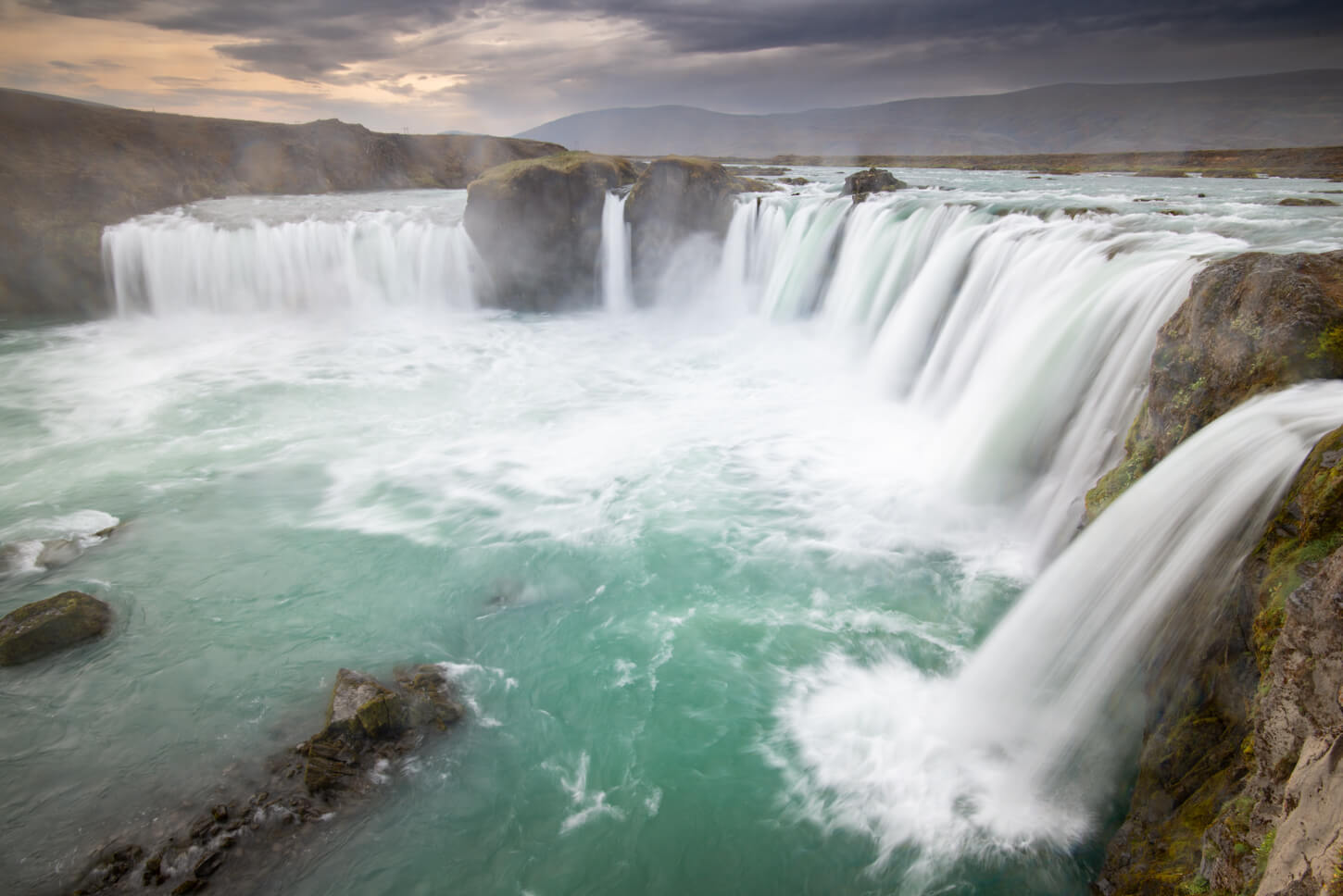close view of a waterfall with multiple streams cascading into the river below, under a dramatic, dark sky