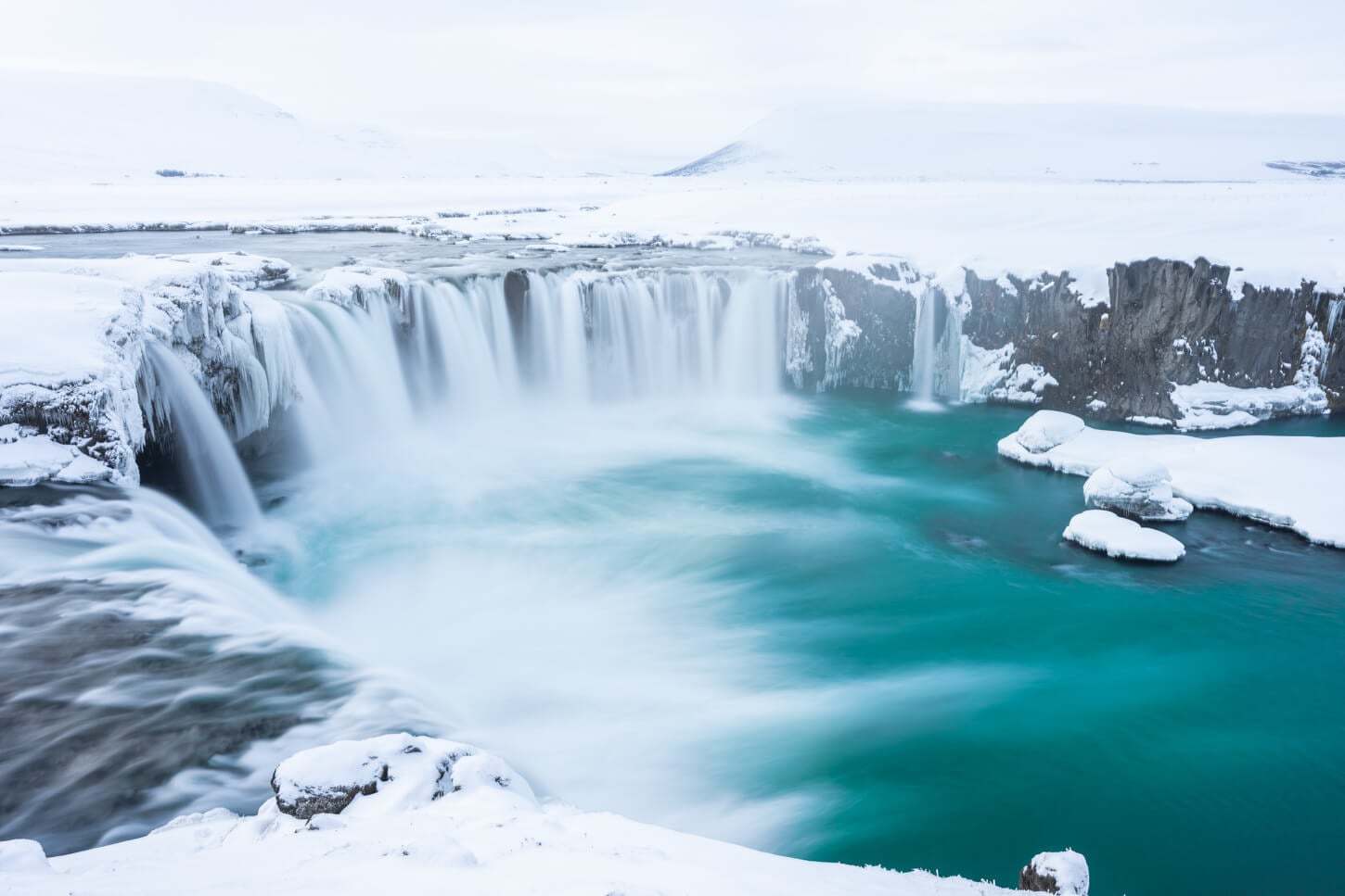 GWatrfall in north iceland with deep blue water, blanketed under the snow and a whiteout, misty sky